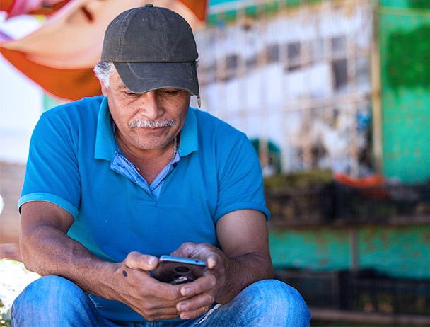 一名男子戴着帽子，穿着蓝色polo衫，坐在商店外面看他的智能手机